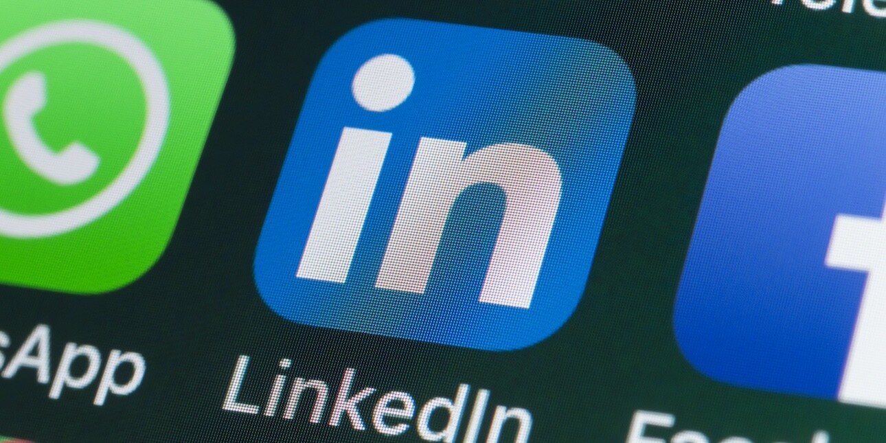 A black screen displaying the linkedin logo which consisting of a blue square with the letters in in white type. Glimpses of other apps surround it.