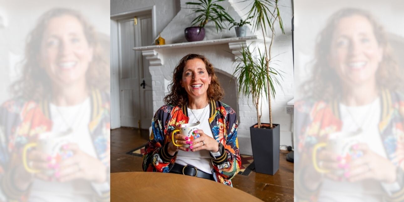 A tryptic of Katie Marlow sat in a chair holding a mug. Katie is a white woman with curly brown hair. She wears a multi-coloured floral jacket. She is sat a table in front of a white brick fireplace and doors