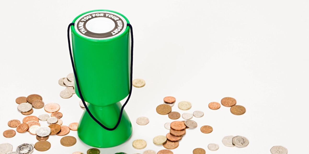 A green charity collection box sits on a white background with coins scattered all aournd it