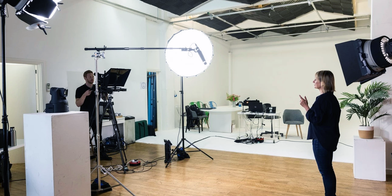 A woman dressed in black standing in front of a camera with a camera operator in a studio