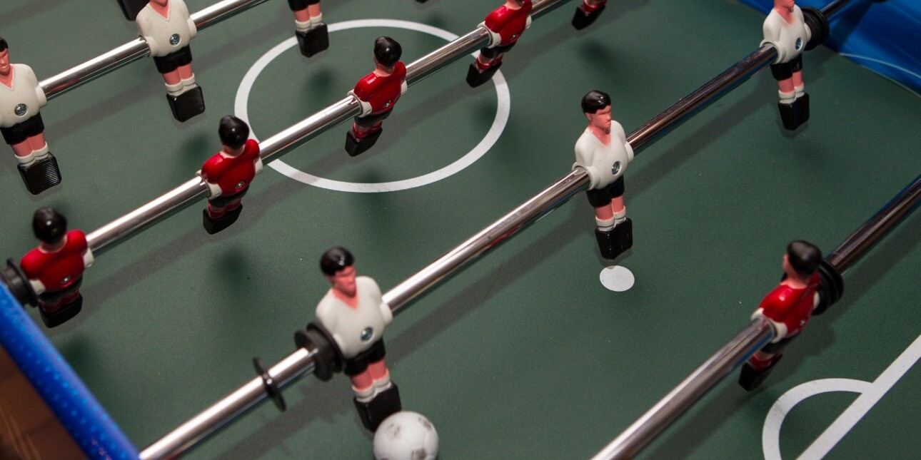 A bird's eye view of table football. The ball is placed at the foot of the right hand striker with the opposing goal keeper poised to defend.