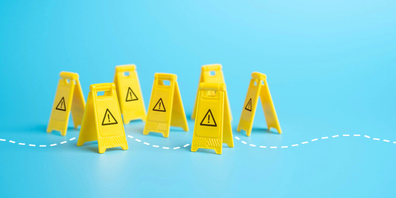 A computer generated image of seven yellow plastic A-boards with black printed exclamation marks on the front. They are placed in random position. A wavy, white dashed line denotes a path through them. The floor and background is bright blue.