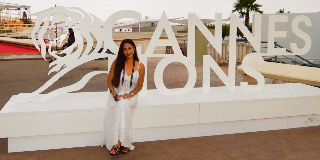 Under a light grey sky Leticia Callista sat in front of a cut out of the words Cannes Lions. In the background are palm trees and assorted conference buildings.