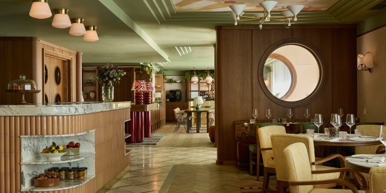 A dining space with pastel coloured bar and lamps, tiled floors, would partition with circular porthole and pistachio coloured decorative ceiling.