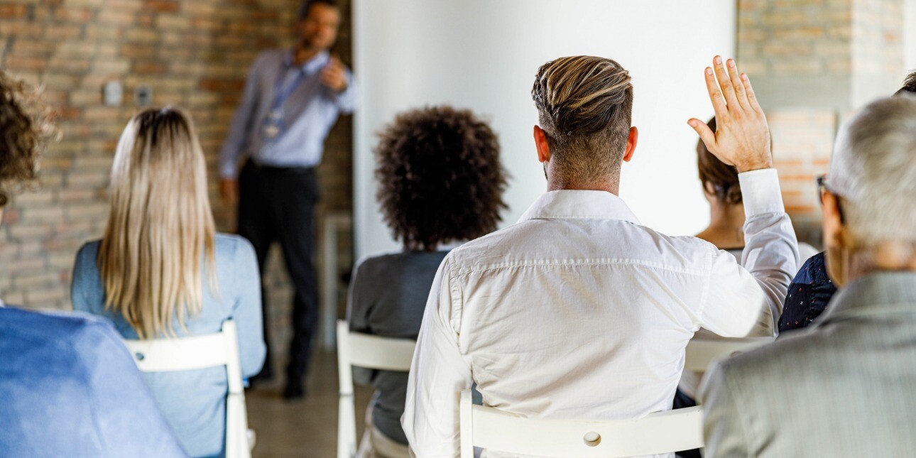 Back view of a man with short blond hair asking a question on a seminar.
