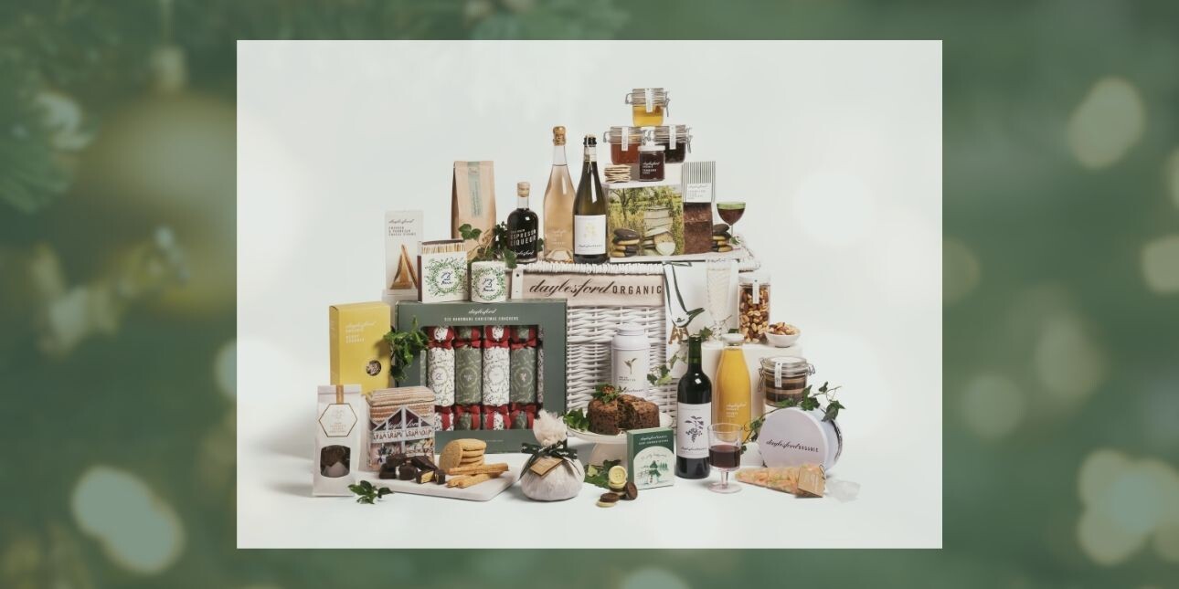 On a green background an image of a Daylesford Christmas wicker hampers surrounded by an assortments of food
