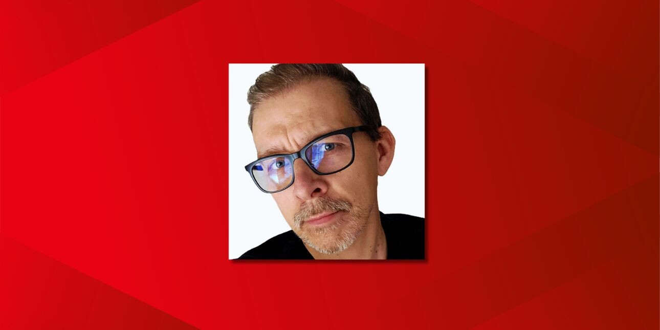 On a red background, a close up colour portrait of Rob Dyson. Rob is a white man with dark hair, glasses and shirt.