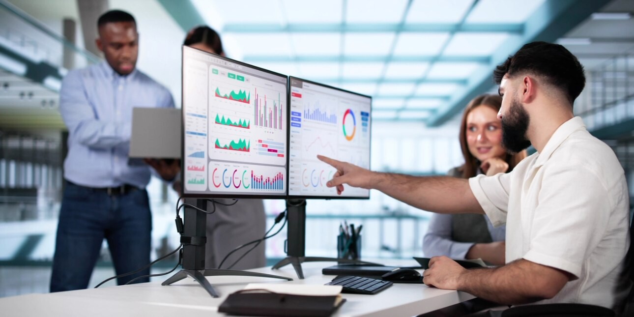 In a modern office a man and woman look at a dashboard on a computer screen while two other colleagues are stood nearby.