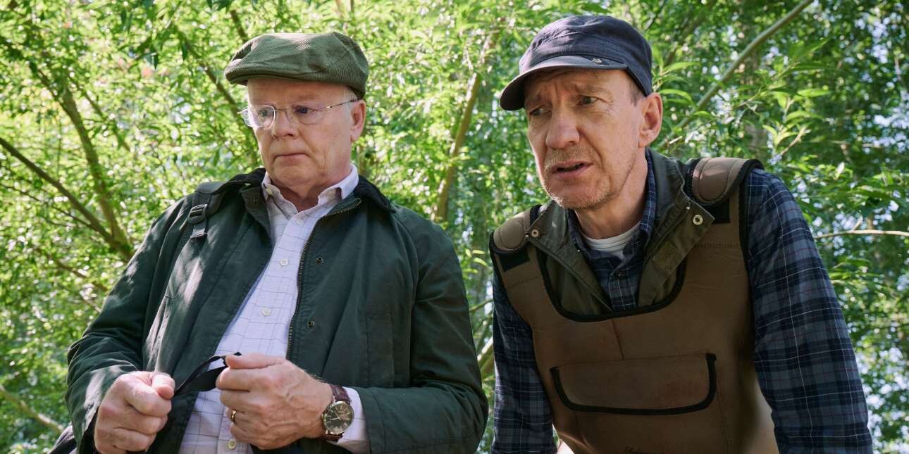 Against a backdrop of leafy trees the actors Peter Hammond and Jason Watkins are photographed in character looking at something out of shot.