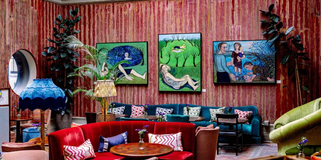 A red walled room furnished with sofas and furnishings in red, teal, blue and green. Three works of art hang from the wall.