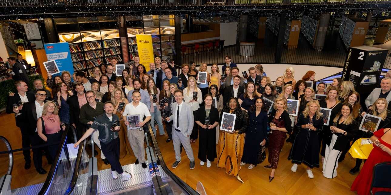 A photograph taken from the top of an escalator of dozens of smiling people holding framed certificates.