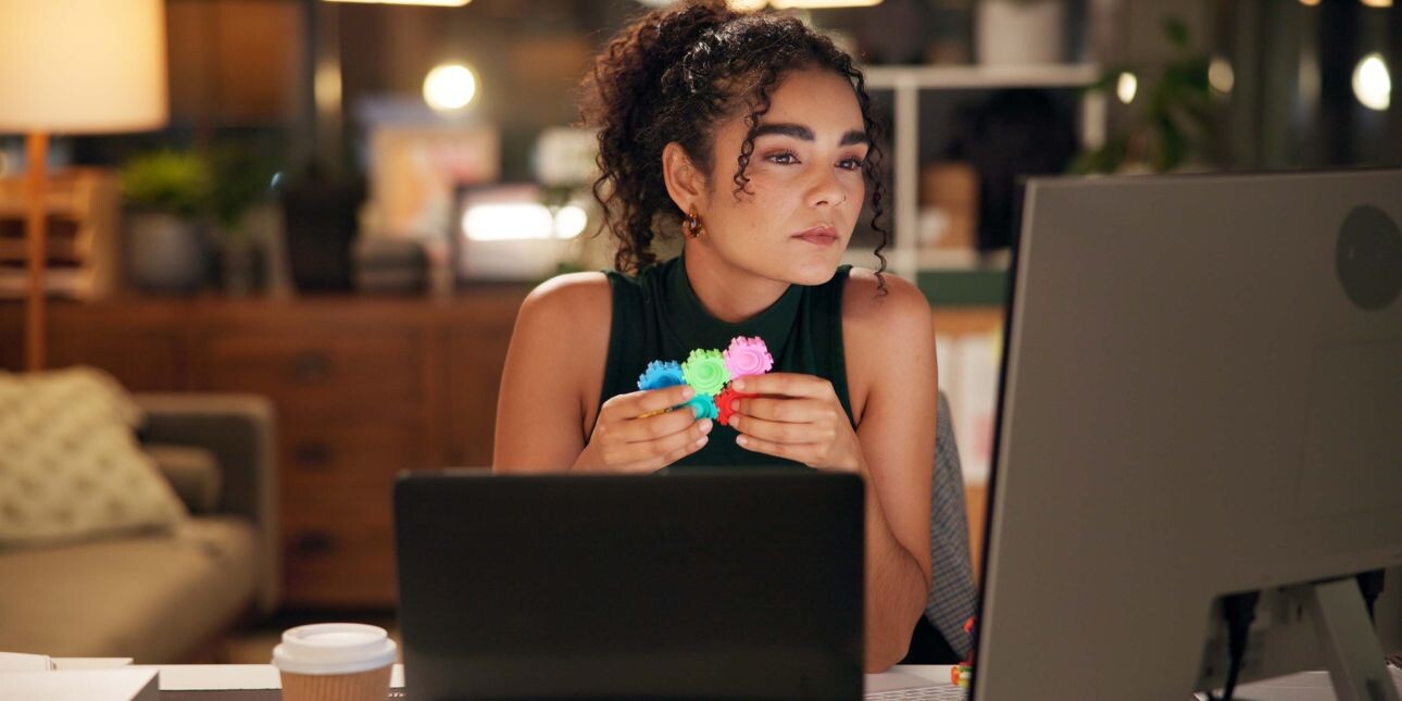 A woman with dark hair and black sleeveless top sat in front of a computer screen holding a fidget spinner.