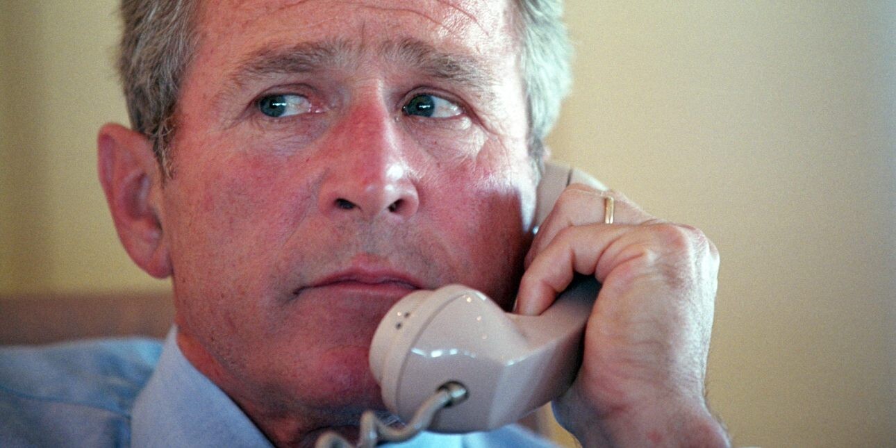 A close up of George W Bush holding a telephone handset to his left ear.