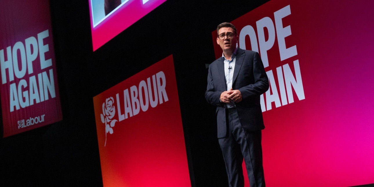 Andy Burnham on stage against a pink-red backdrop.