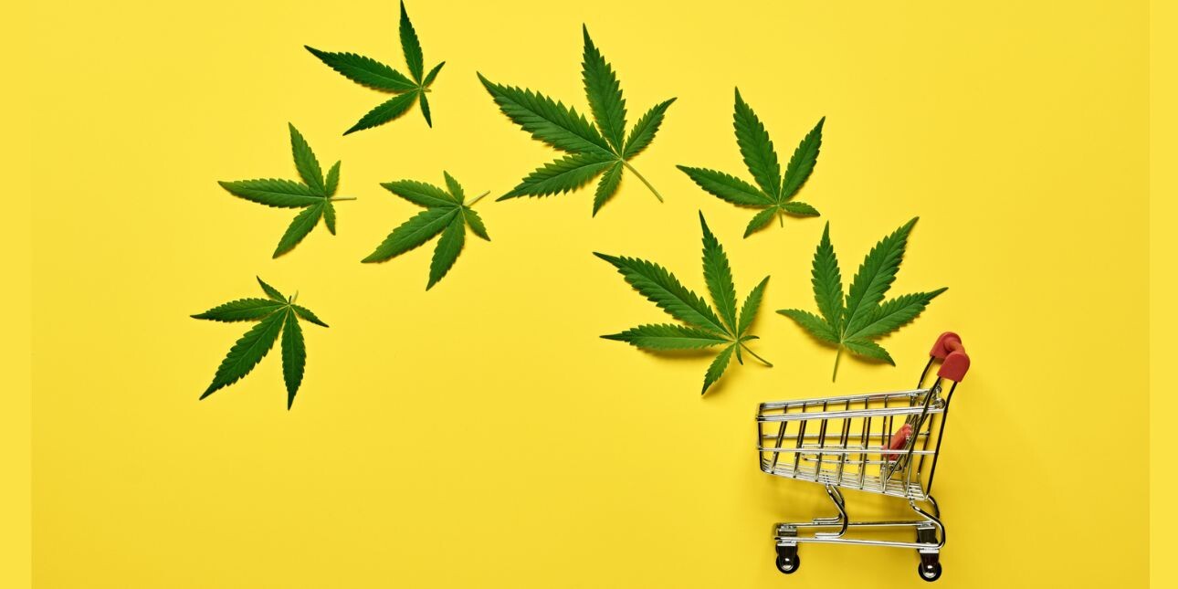 On a yellow background, eight cannabis leaves floating above a shopping trolley.