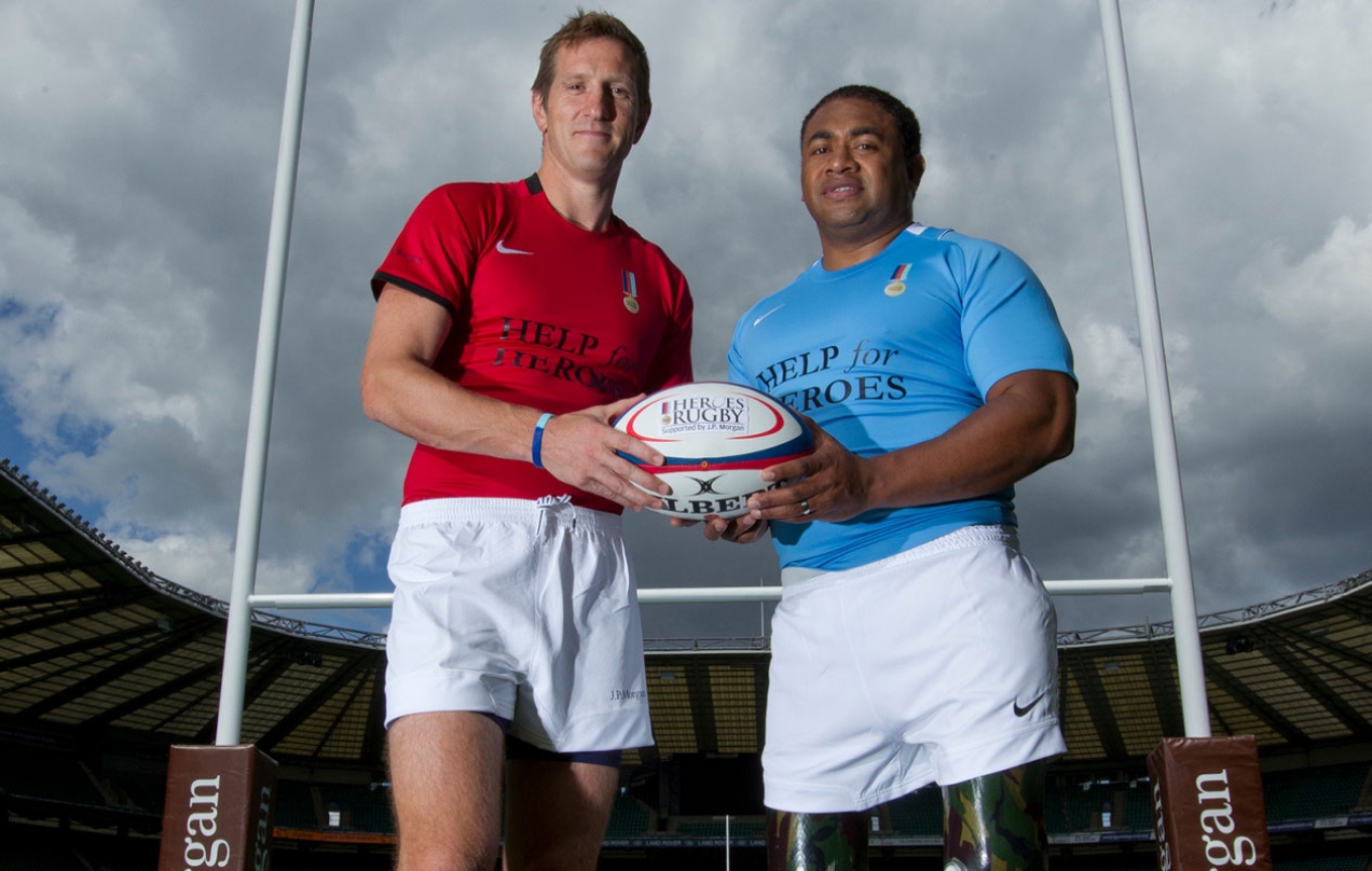 Two rugby players looking at the camera holding a rugby ball.