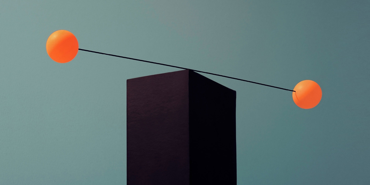 A rod with two yellow spheres attached to it is balancing on the edge of a black brick – getting the right balance.