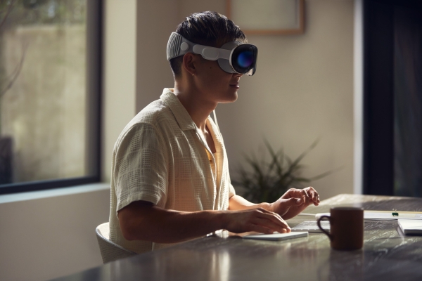 A man sits at a desk while wearing an Apple Vision Pro headset