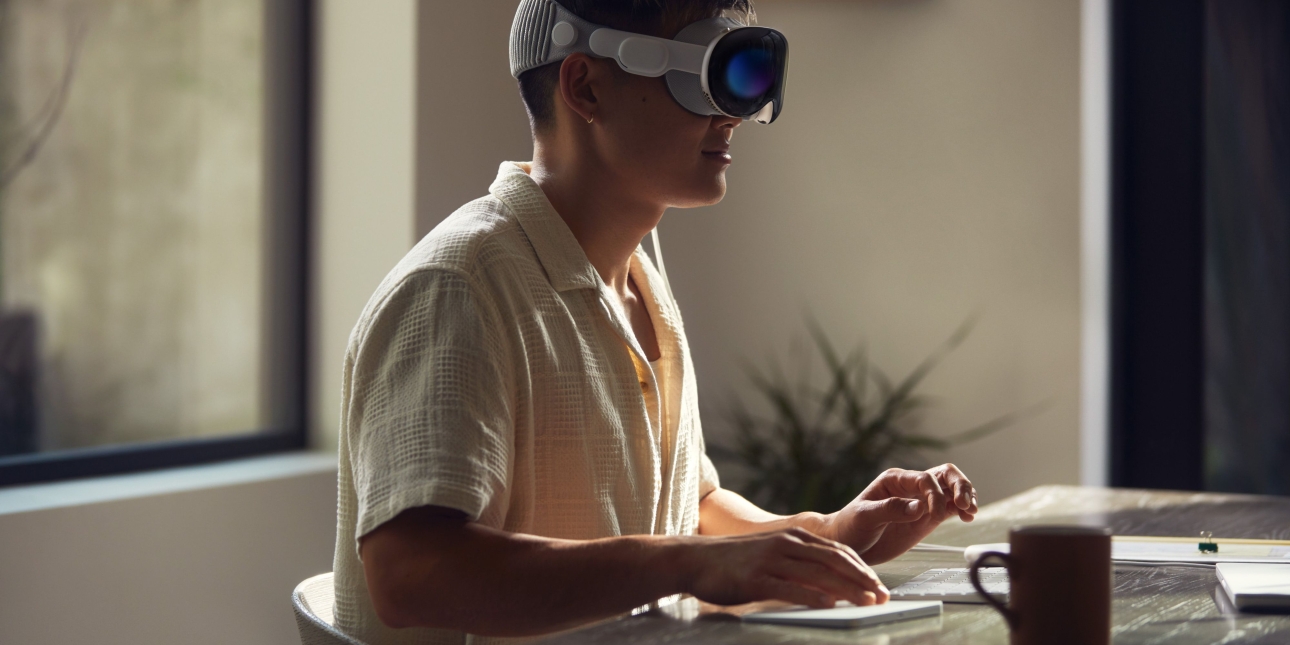 A man sits at a desk while wearing an Apple Vision Pro headset