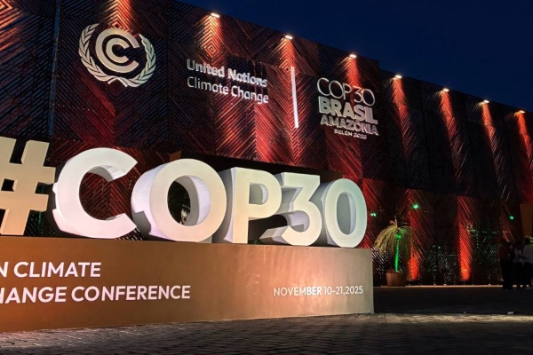 Lit up against a dark night's sky, a three-dimensional typographic sculpture featuring a large hashtag COP30 on a plinth in front of the main entrance venue in Belém, Brazil. Various logos feature in white.