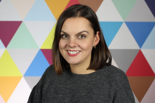 Carly Bannerman, a white woman with dark shoulder length hair, on a background of multicoloured triangles