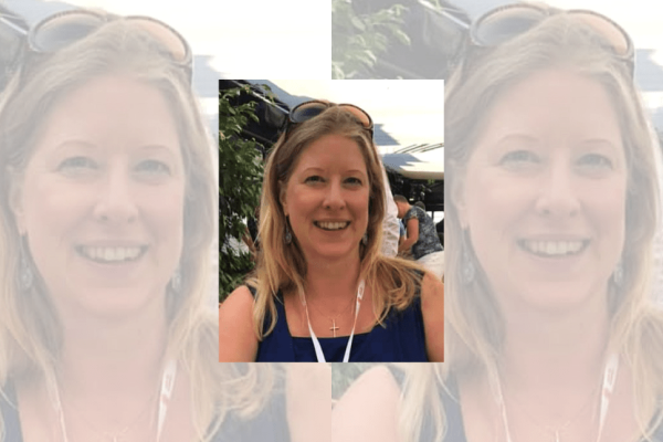 A portrait of Caroline Klein with mountains in the background. Caroline is a blonde white woman wearing a blue vest top with sunglasses on her head and a white lanyard.