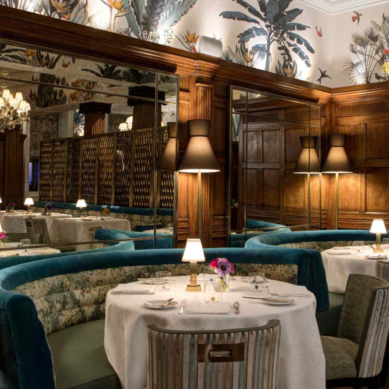 Round tables draped in cloths surrounded by three semi-circular seating benches in turquoise material. Wooden panelling gives a sense of intimacy