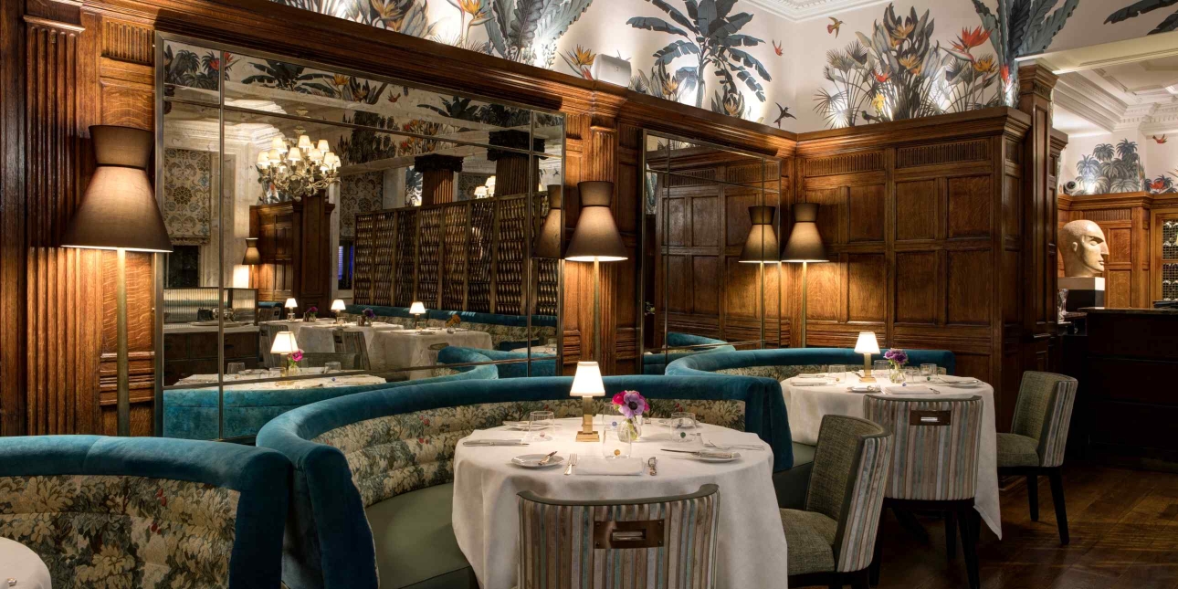 Round tables draped in cloths surrounded by three semi-circular seating benches in turquoise material. Wooden panelling gives a sense of intimacy