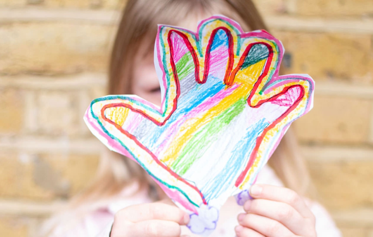 Young girl holding a hand drawn hand in front of her face. 