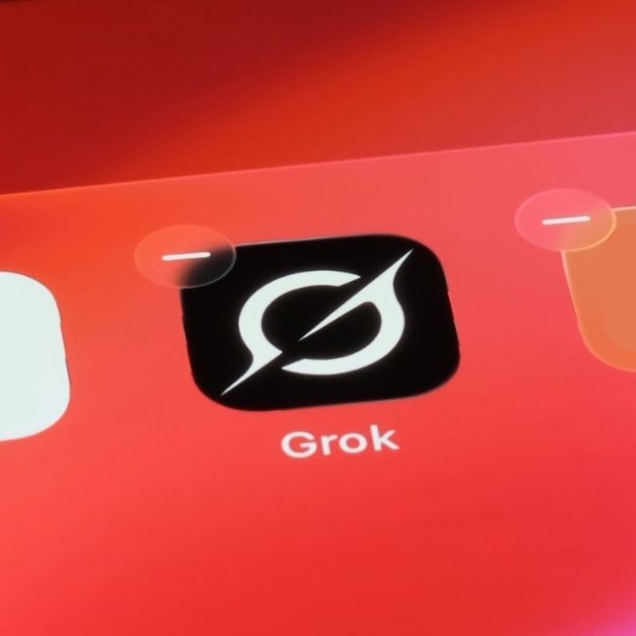 A photo of the Grok app on a pink-orange mobile phone screen. The Grok logo is a white stylised uppercase G on a black background.