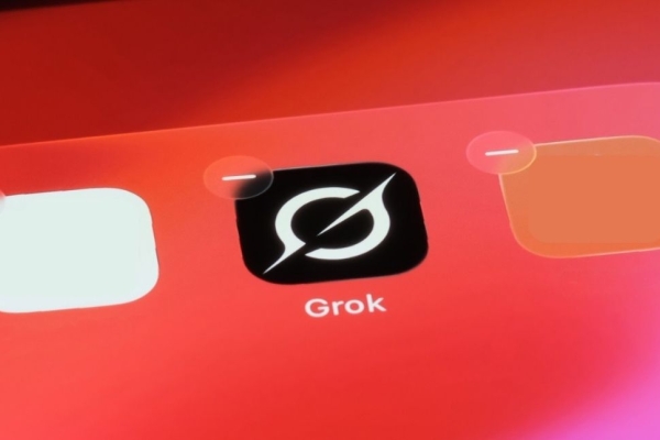 A photo of the Grok app on a pink-orange mobile phone screen. The Grok logo is a white stylised uppercase G on a black background.
