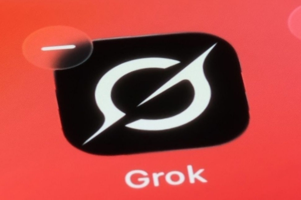 A photo of the Grok app on a pink-orange mobile phone screen. The Grok logo is a white stylised uppercase G on a black background.