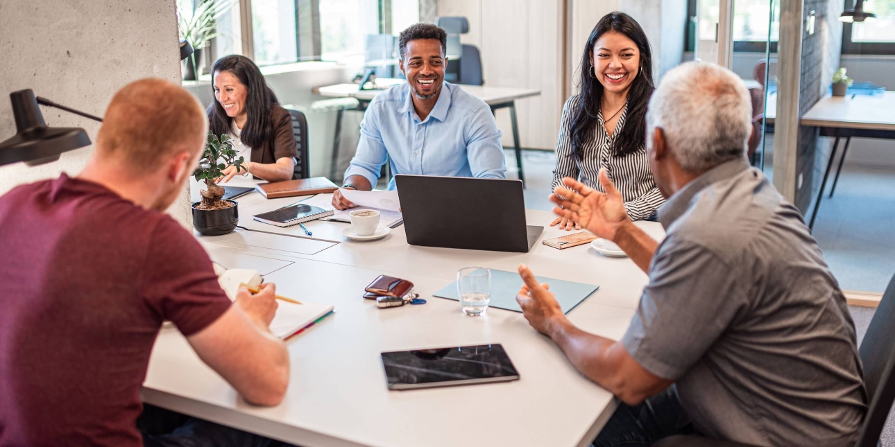 A group of five colleagues of different genders, ages and ethnicities chat around a table: