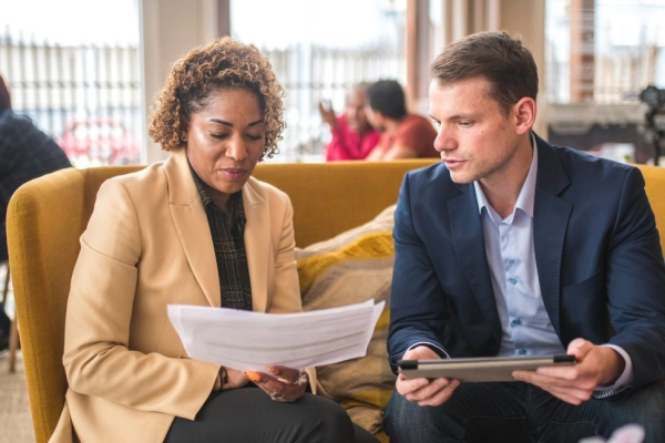 Two colleagues sat on a yellow sofa discussing paperwork