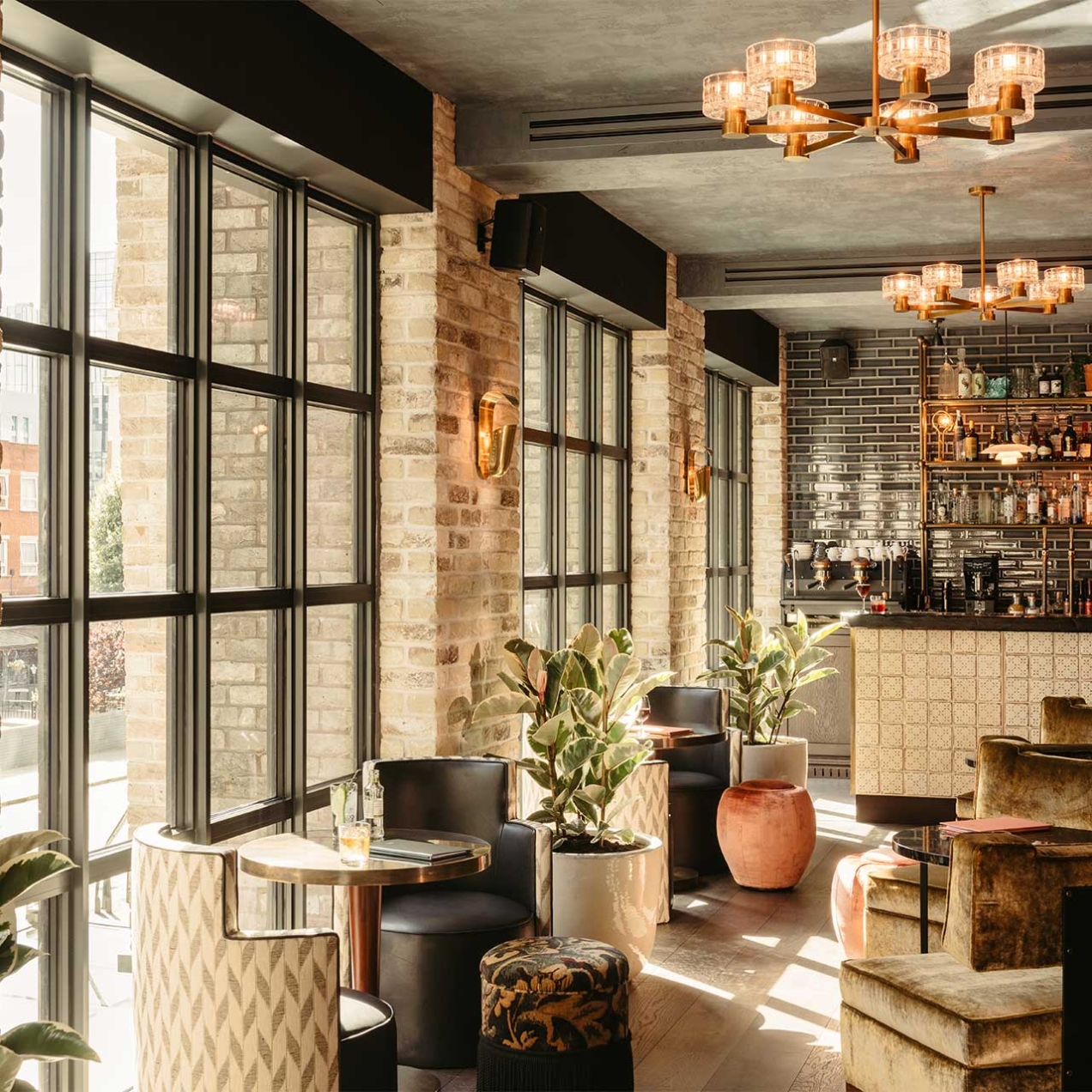 The Hoxton in Southwark - room shows tables and chairs beside a big window plants and lights and a bar in the background
