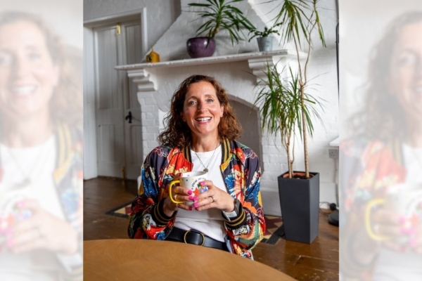 A tryptic of Katie Marlow sat in a chair holding a mug. Katie is a white woman with curly brown hair. She wears a multi-coloured floral jacket. She is sat a table in front of a white brick fireplace and doors