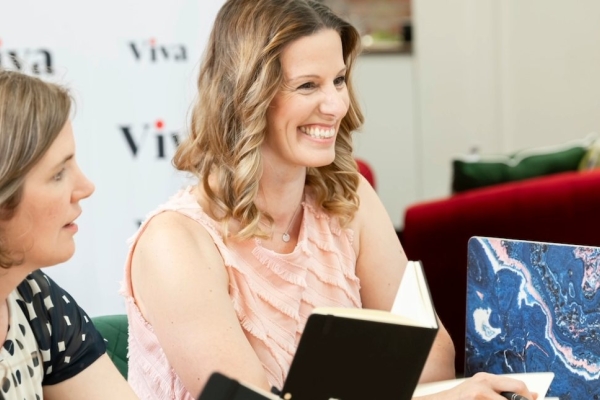 A smiling Lisa Egan-Woodhouse sat among members of the Viva team. Egan-Woodhouse is a white woman with shoulder length light brown hair, who is wearing a pink sleeveless top.