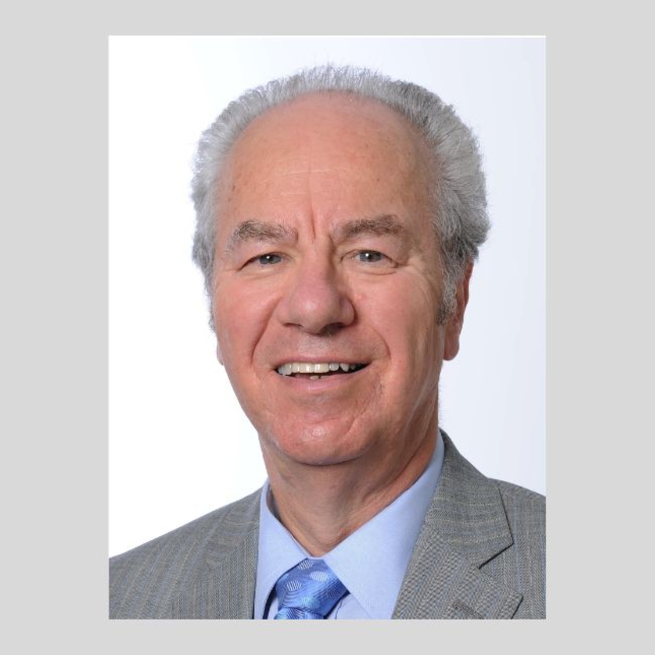 On a grey background, a colour photograph of Peter Kellner. He is a white man with grey hair, grey suit, blue shirt and blue tie.