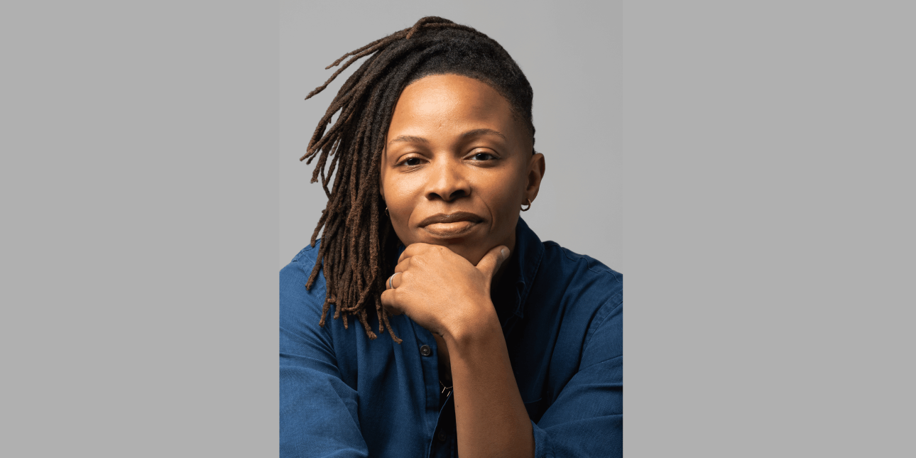 Prentis Hemphill, a black person with shoulder length hair and blue top, holds their chin in their left hand while looking at the camera