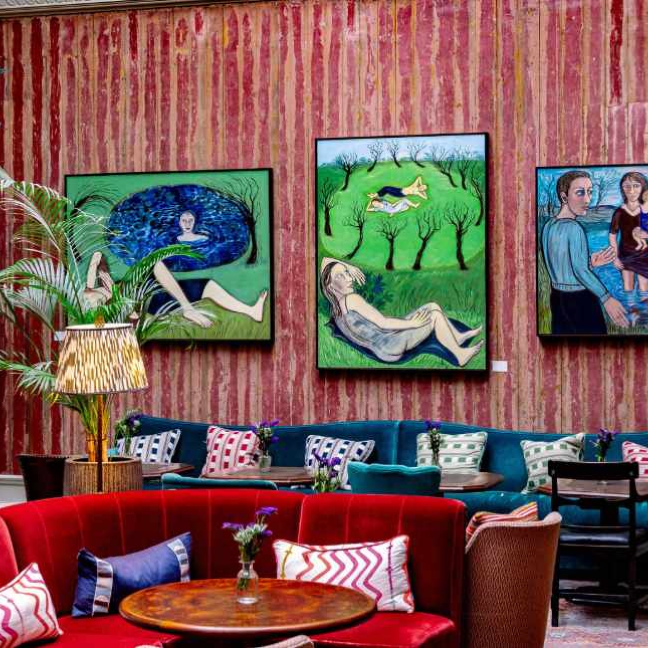 A red walled room furnished with sofas and furnishings in red, teal, blue and green. Three works of art hang from the wall.