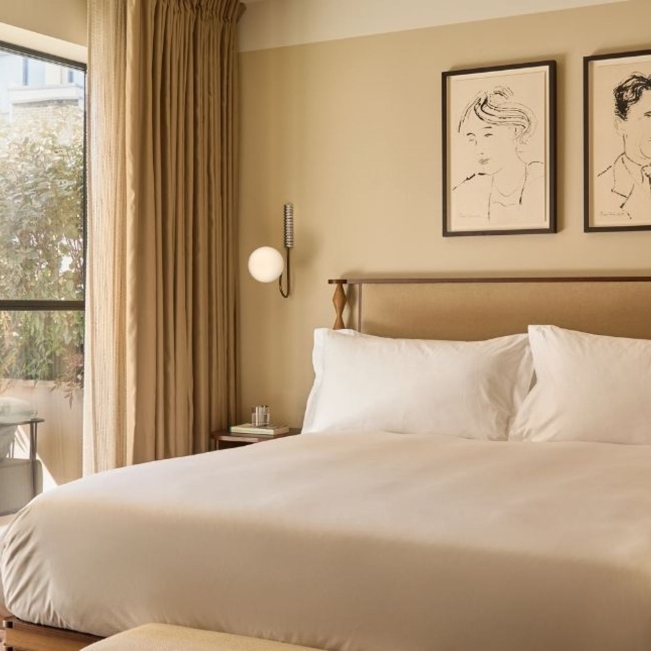 An exquisite hotel room furnished in cream shades with a large bed, pictures and doors to a terrace.