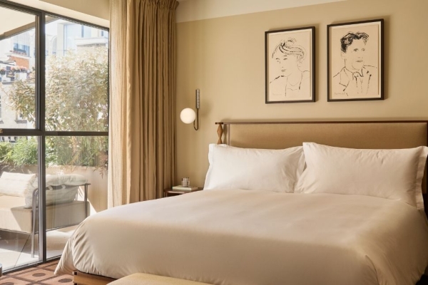 An exquisite hotel room furnished in cream shades with a large bed, pictures and doors to a terrace.