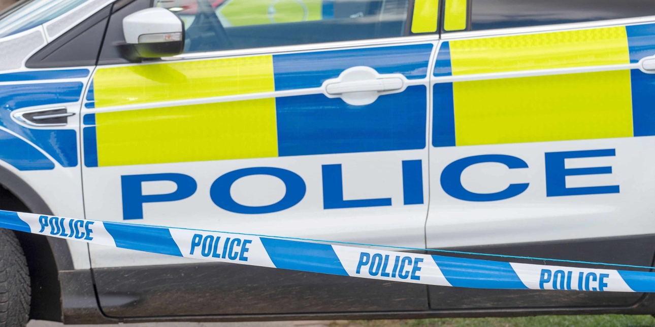 Close up shot of a police car door with blue and white police tape in the foreground