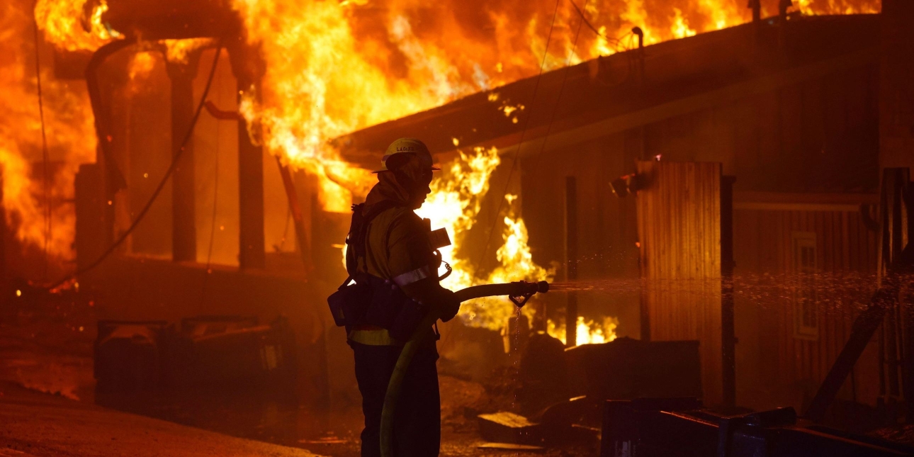 The silhouetted figure of a firefighter holding a hose to douse the flames which have engulfed a building