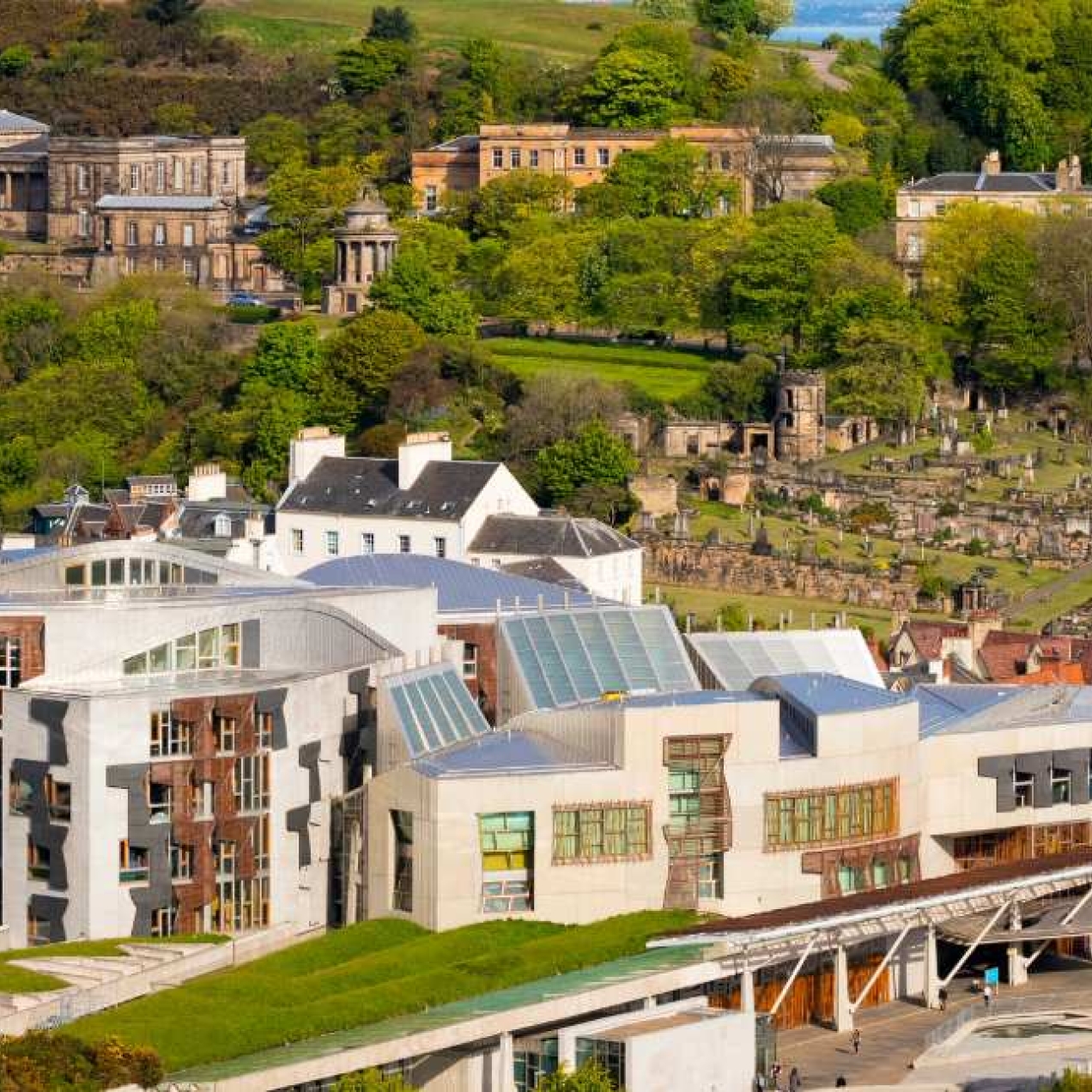 An aerial photograph with the modern Scottish parliament in the foreground and other historic buildings among the greenery in the background