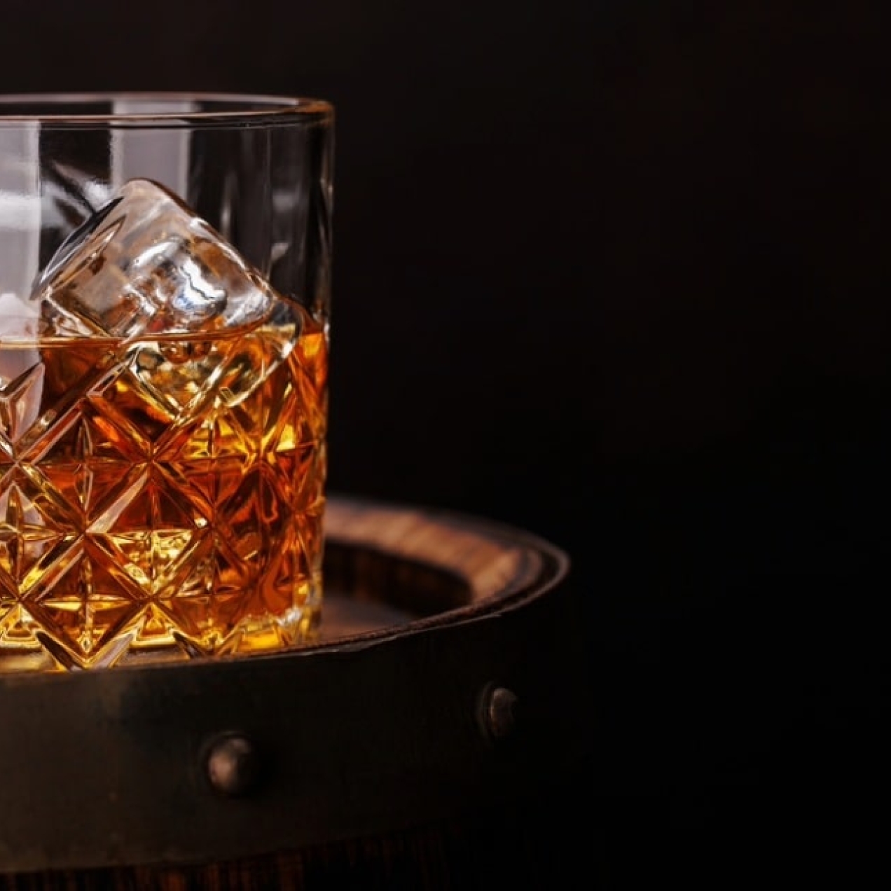 On a black background a glass of whisky stood on the top of an aged barrel.