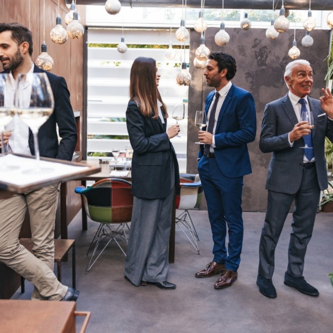Five professionals of different ages holding wine glasses while networking in a modern event space