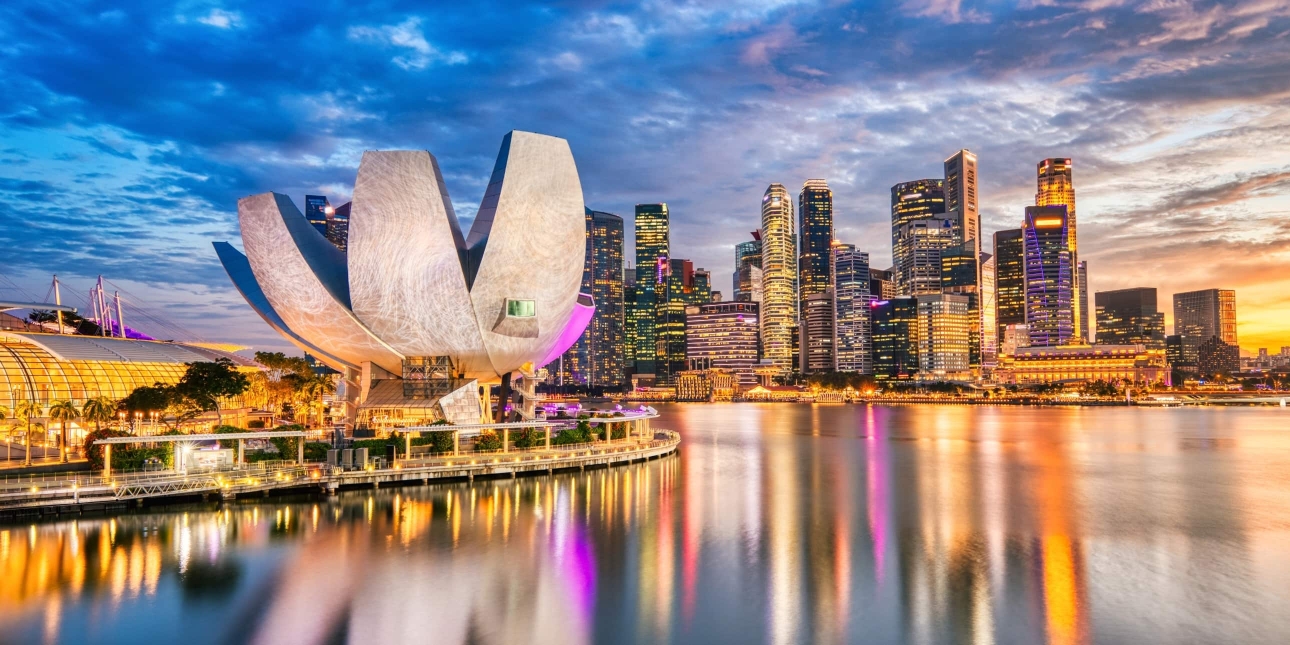 The Singapore city skyline at dusk viewed from Marina Bay with the tulip-shaped ArtScience museum in the foreground and skyscrapers in the background