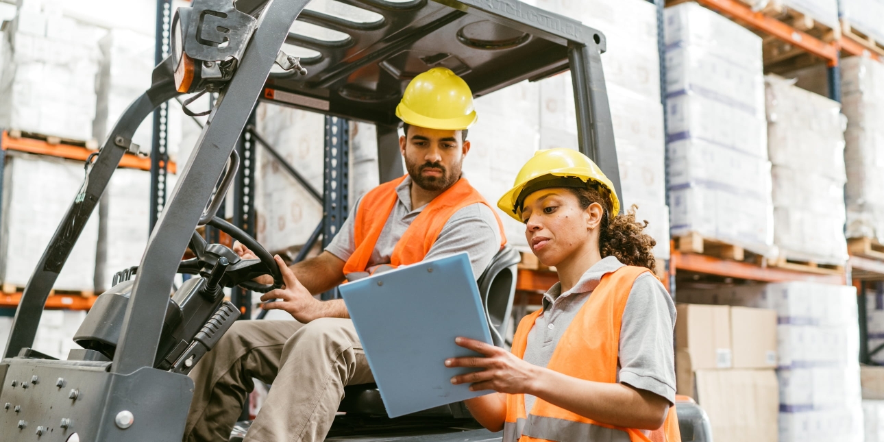 A woman warehouse manager giving instructions to a male forklift operator