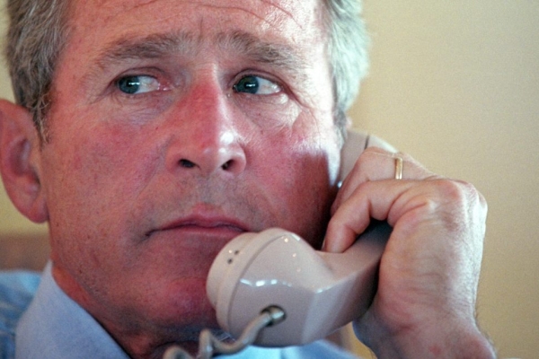 A close up of George W Bush holding a telephone handset to his left ear.